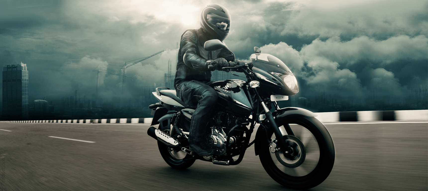A biker is riding black and blue color Bajaj Pulsar 150cc motorcycle wearing black leather jacket and helmet in open road